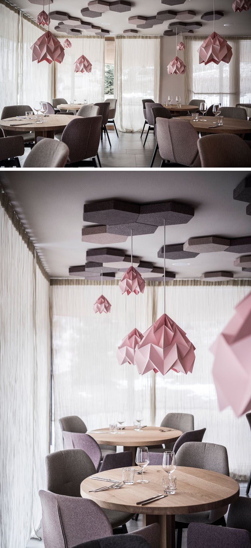 The contemporary pink light fixtures hanging from honeycomb details are the focal point in this modern hotel restaurant. Round wood tables, with dusty pink and gray wool upholstered chairs help to create a cozy atmosphere. 