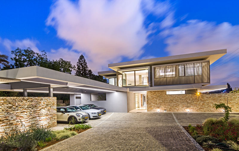 This modern house has a stone driveway that opens up to a parking area with carport on the left and visitor parking on the right.