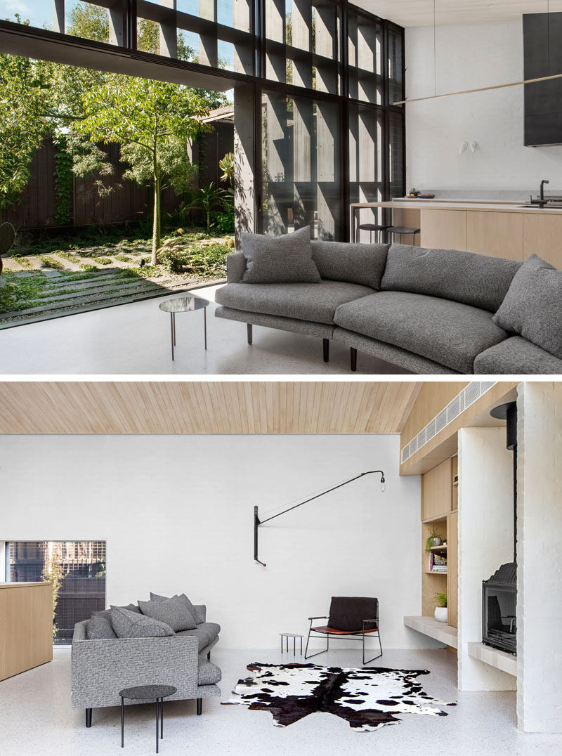 This modern living room that opens to a small sculptural backyard, has a grey curved couch that's positioned to view the black fireplace.