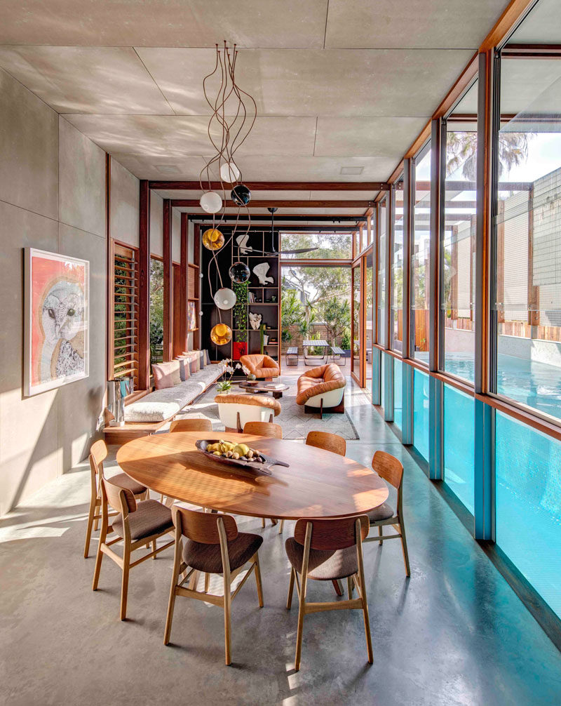 Sculptural lighting hangs from the ceiling above the oval dining set featured in this modern house. The wood furniture compliments the wood window frames and louvers.