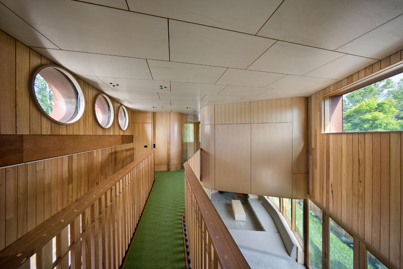 Green flooring adds a touch of color to the mostly wood interior of this modern house, while circular and rectangular windows let natural light in.