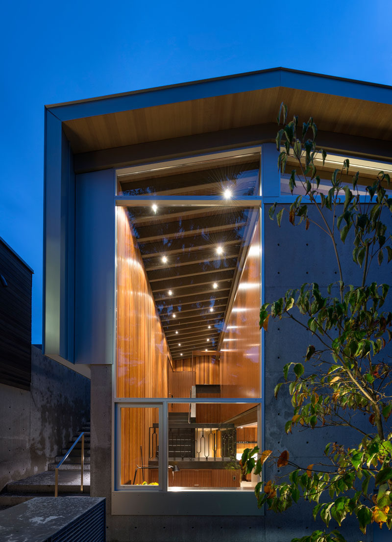 At the side of this modern waterfront house, there's a glimpse of the interior showing the stairs with a decorative railing, the study and the wood interior.