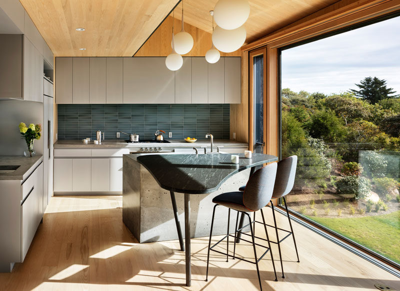 This modern kitchen has matte light grey cabinets and a curved island with space for seating. A large picture window perfectly frames the view.