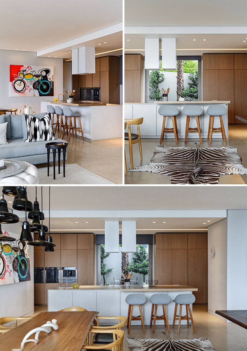 This modern kitchen has a large white island with wood bar area, and floor-to-ceiling wood cabinets with a large framed window.