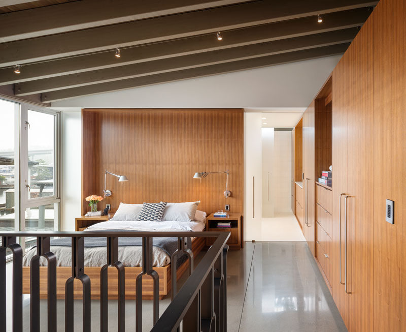 In this modern and open master bedroom, wood cabinets and closets line the wall and opposite is a wall of windows. Wood is also used as a feature headboard and as the frame for the bed.