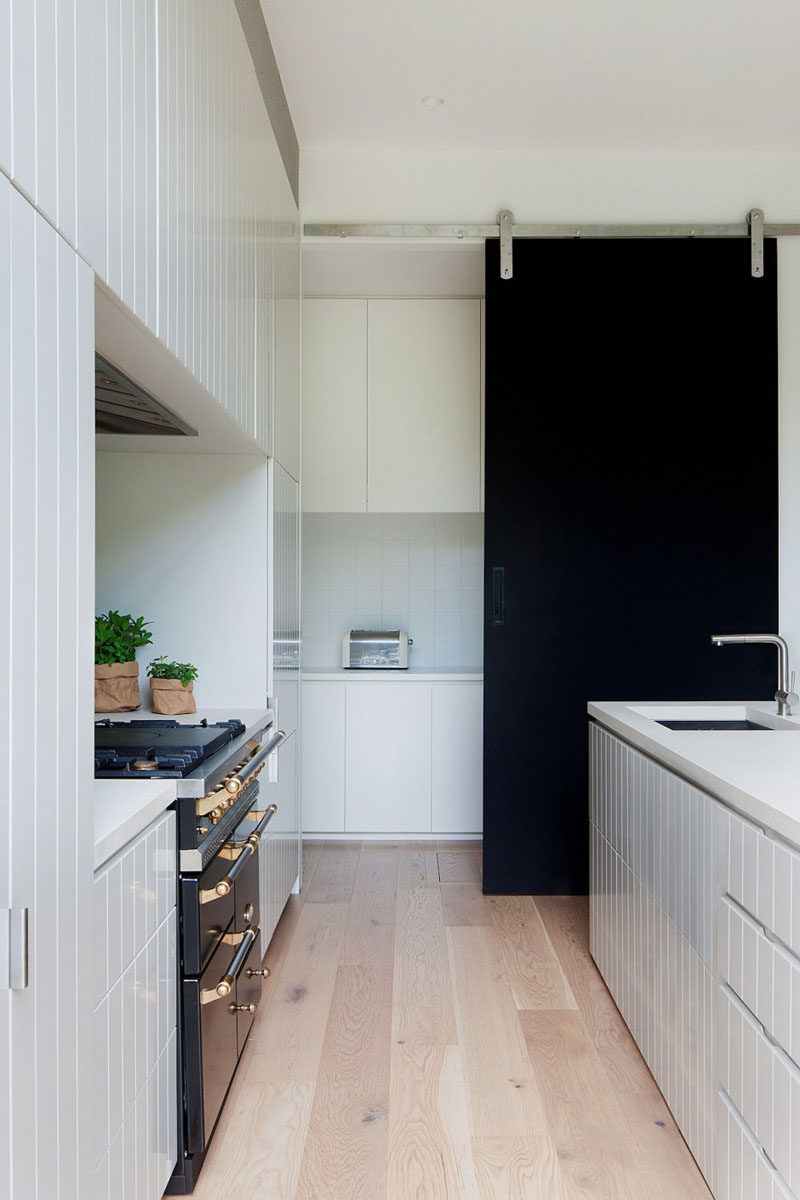 The black sliding barn door in this modern kitchen creates a bold contrast against the all white cabinetry and light wood flooring.