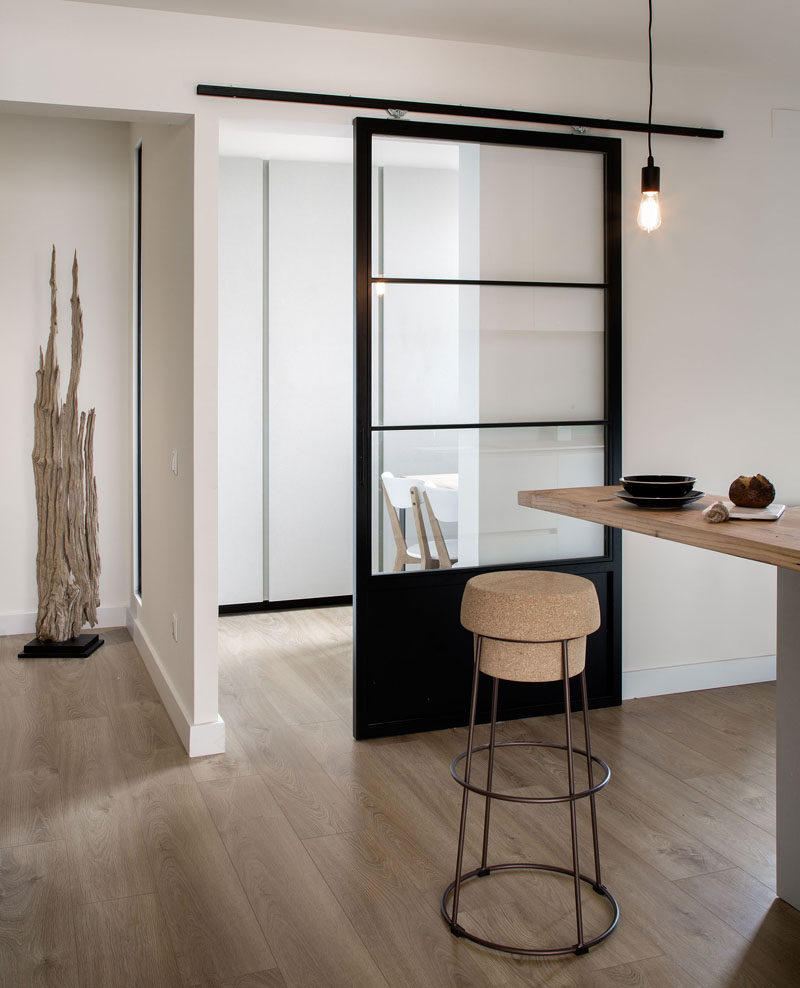 This glass and black sliding door separates the main part of the kitchen from a dining area and gives the space a modern industrial look that's accentuated by the exposed hanging bulb and metal bar stool.