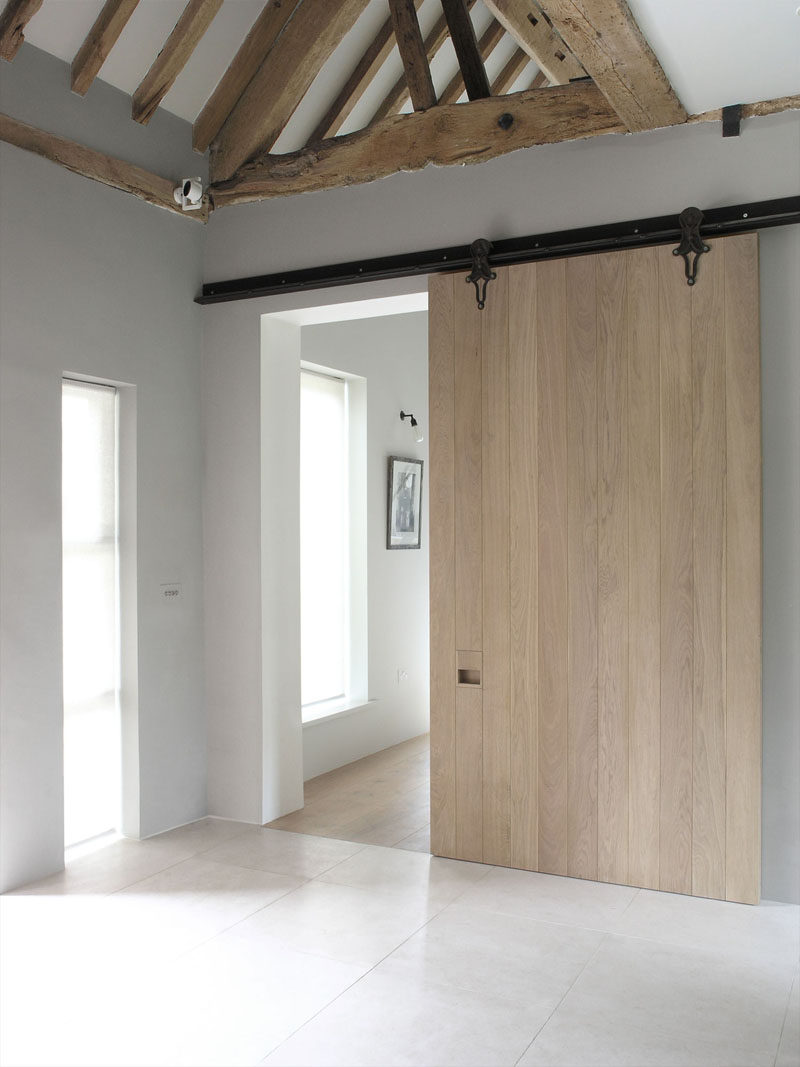 This large sliding barn door made from light wood and a dark metal rail creates a contemporary look in this remodeled home that maintained some of the original rustic ceiling details.