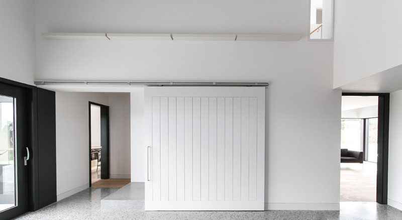 The white sliding barn door in this modern home helps keep the space bright and welcoming, and blends in with the white walls around it.