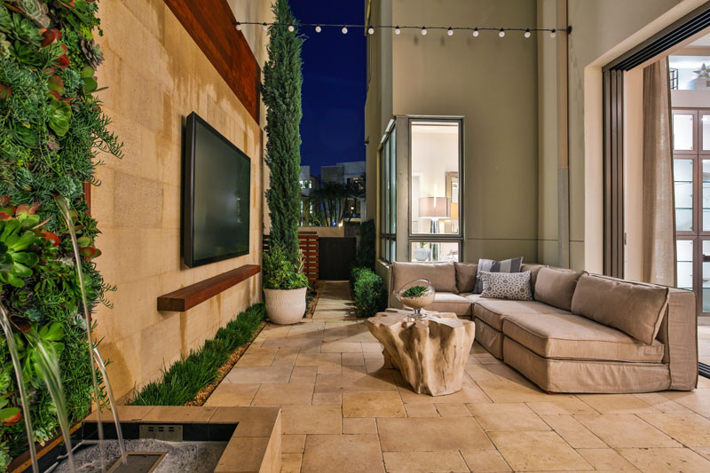 The narrow space on this modern patio is tight but it still manages to comfortably fit a barbecue, a large sofa, a water feature, and a wall mounted TV.