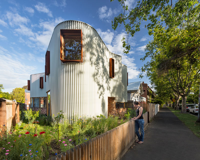 This modern house is covered in a custom made zig-zag metal facade that creates a continuous curving appearance, that sits on top of reclaimed brick and is broken up by rusted steel hoods around the windows.