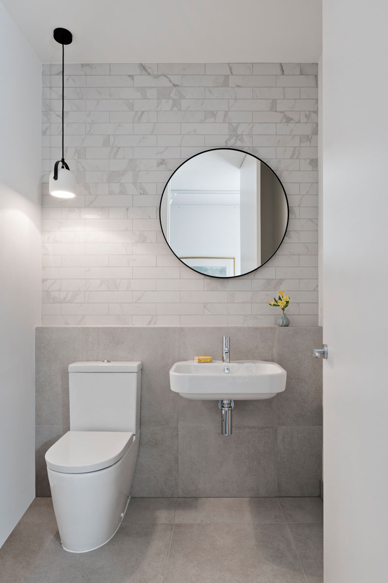 White and light grey tiles line the back wall in this modern bathroom, while a single white and black pendant light hangs above the toilet.