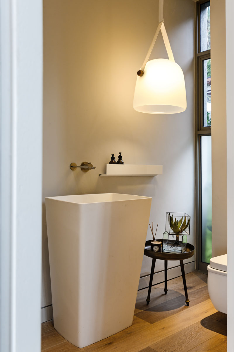 This modern bathroom has an oversized white pendant light, and a large white stand alone sink beside a set of windows. 