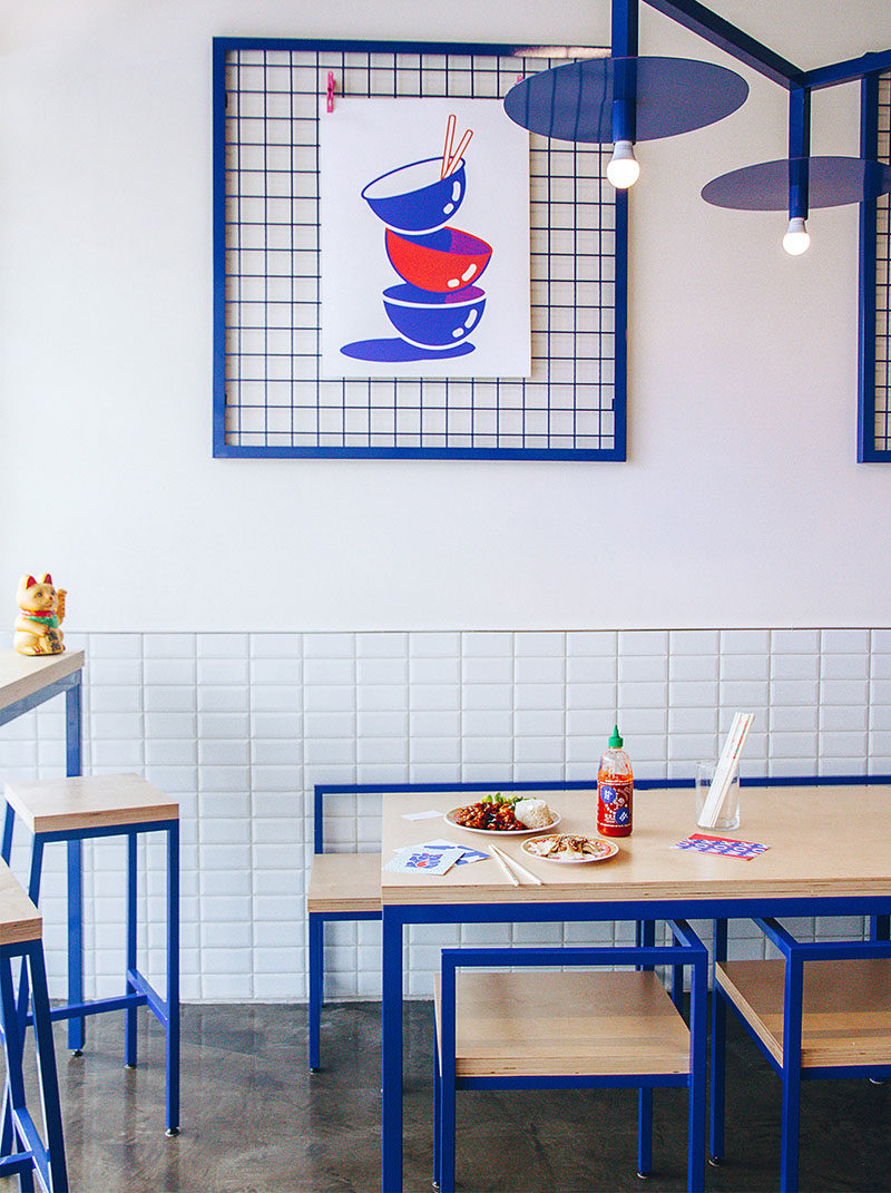 A custom made, blue zig-zag light fixture hangs in the middle of this modern restaurant tying together the overall look of the furniture and decor. White subway tiles partially cover the walls, while blue metal grid frames with graphic artwork, adds a unique decor element that can be easily changed out.