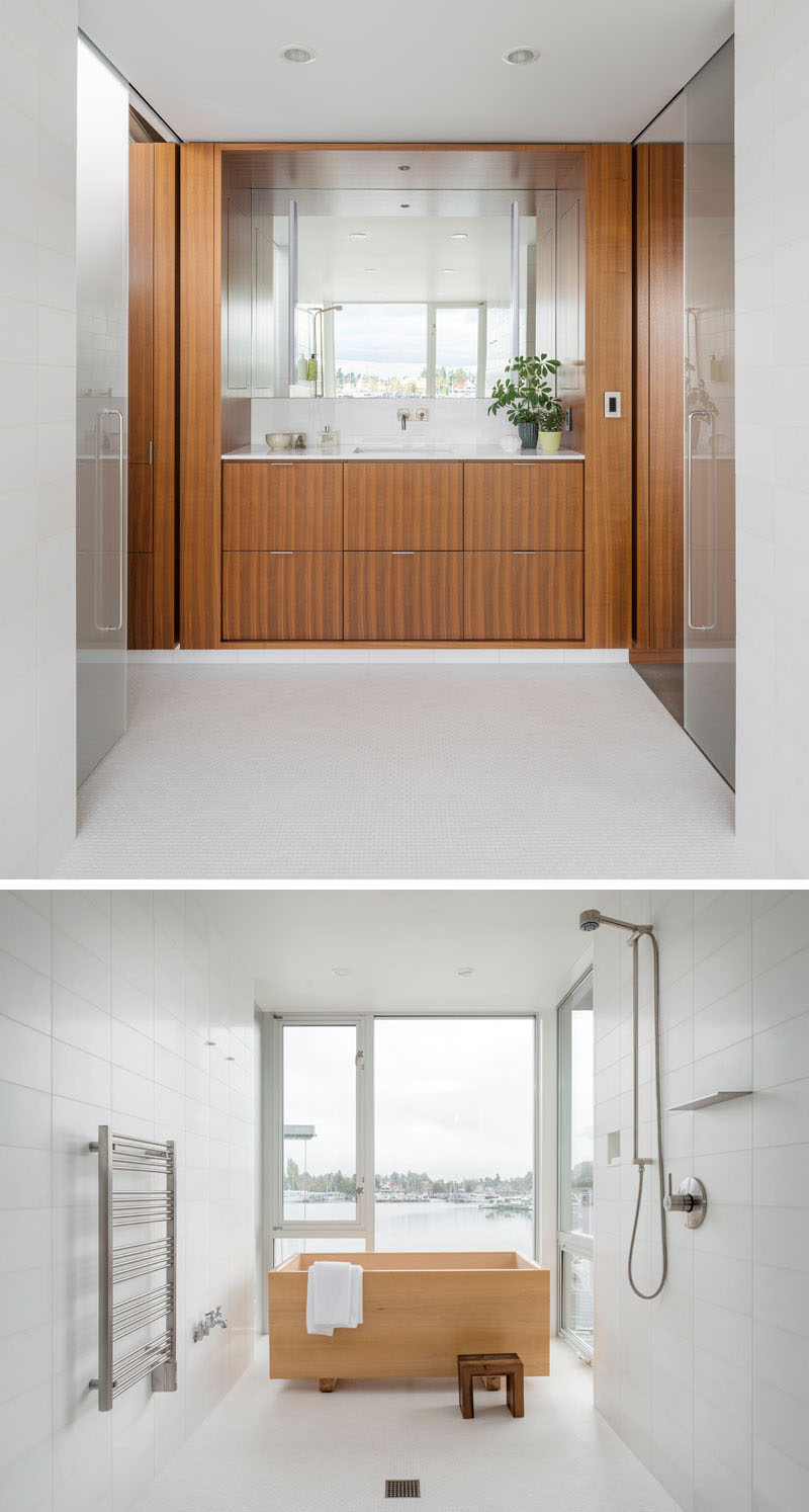 Hidden behind sliding frosted doors is this modern master bathroom. A wood vanity with plenty of storage is topped with white countertops and a large mirror. To the side of the vanity is a shower and a Japanese style hinoki tub (soaking tub) surrounded by white tiles, while large windows overlooks the lake.