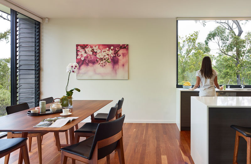 This modern dining room features a simple look, with the wood and black upholstered dining set complimenting the rich wood flooring, while a pop of color is added to the dining area with a pink floral painting. 