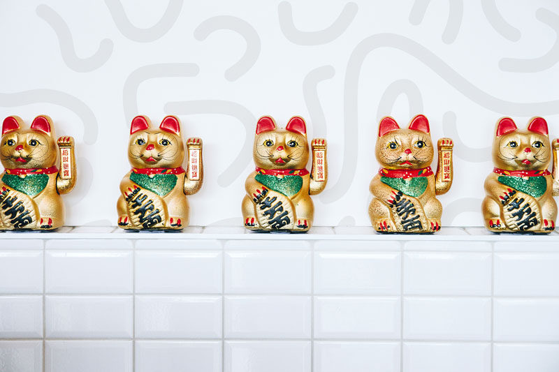 Sticking true to the name of this modern Asian restaurant, mini maneki-neko fortune cat figurines are displayed on a built-in shelf on the front of the white tiled service counter. 