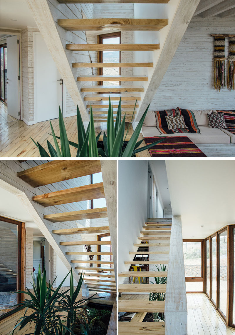 Wood stairs lead up to the upper floor of this modern house, where bedrooms are located. Beneath the stairs is a void in the floor for plants that add greenery to the otherwise light interior.