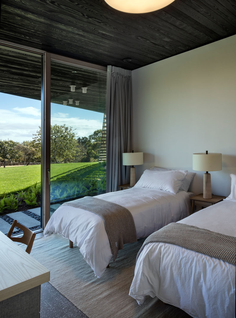 In this modern bedroom, two beds separated by nightstands, have tree views and direct access to the garden.