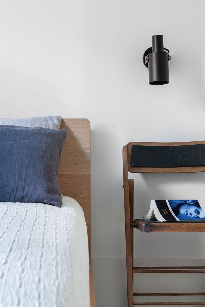 This bedroom has been kept simple in its design with white walls and wood elements, like the bed frame and chair that is being used as a nightstand.