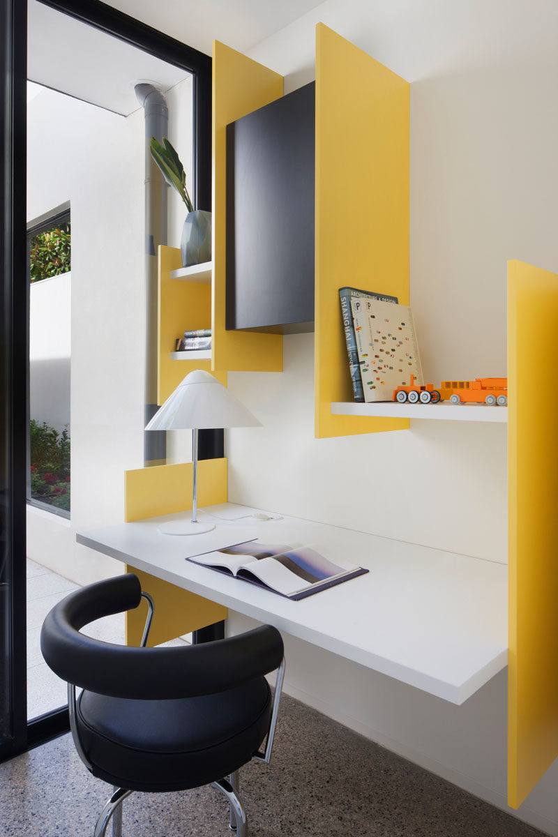 This small and modern study has bright yellow supports that hold the white wall shelves and floating desk in place.