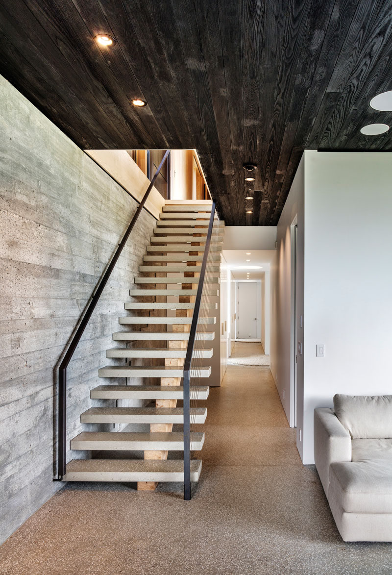In this modern house, the ceiling contrasts the board formed concrete wall, the lightly colored stairs and the white hallway.