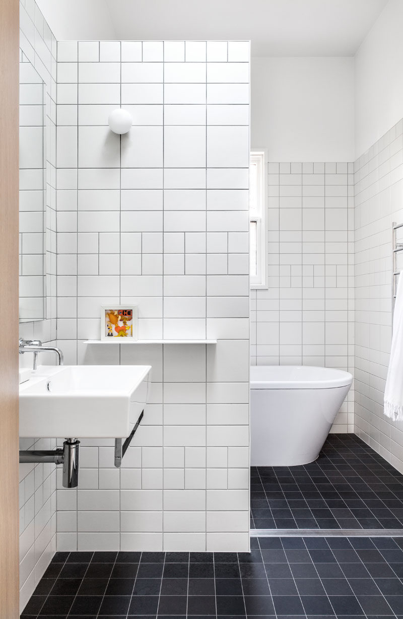 In this modern and simple bathroom, white tiles in different sizes have been used for the walls, while black tiles have been used for the floor.