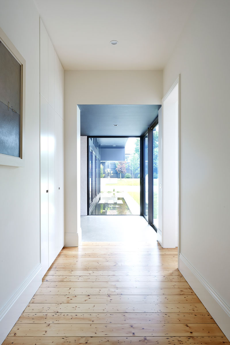 This white hallway has wood and concrete flooring. The wood flooring is from the original house, while the concrete floor is in the new modern extension.