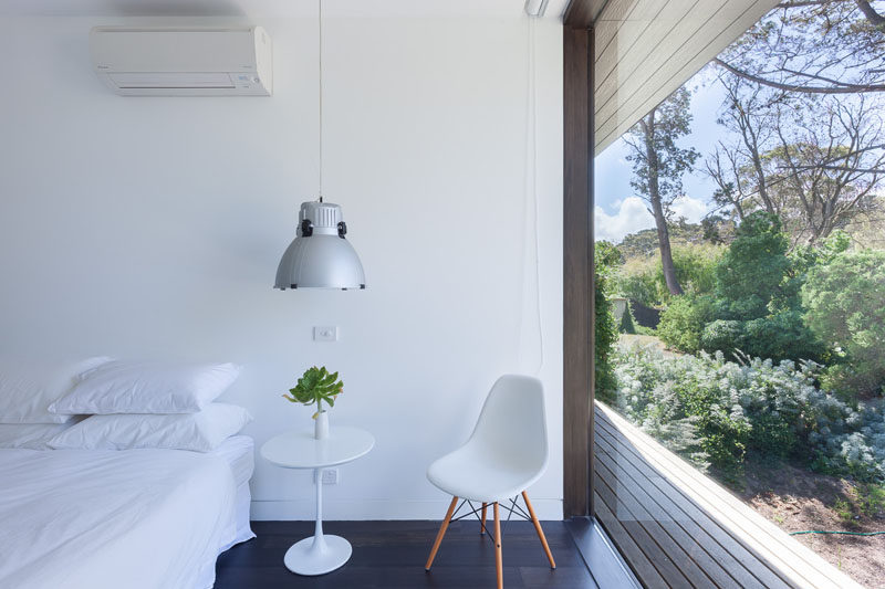 This modern bedroom is simply decorated in white with dark hardwood floors, this room with a large floor to ceiling window, has a beautiful view of the vegetation at the front of the house.