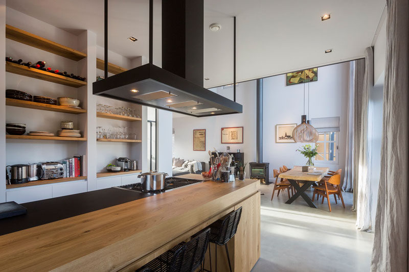 This modern kitchen has light wood island with a built-in stove and space for seating is the focal point in this room. Exposed wood shelving on the wall makes housewares easy to reach.