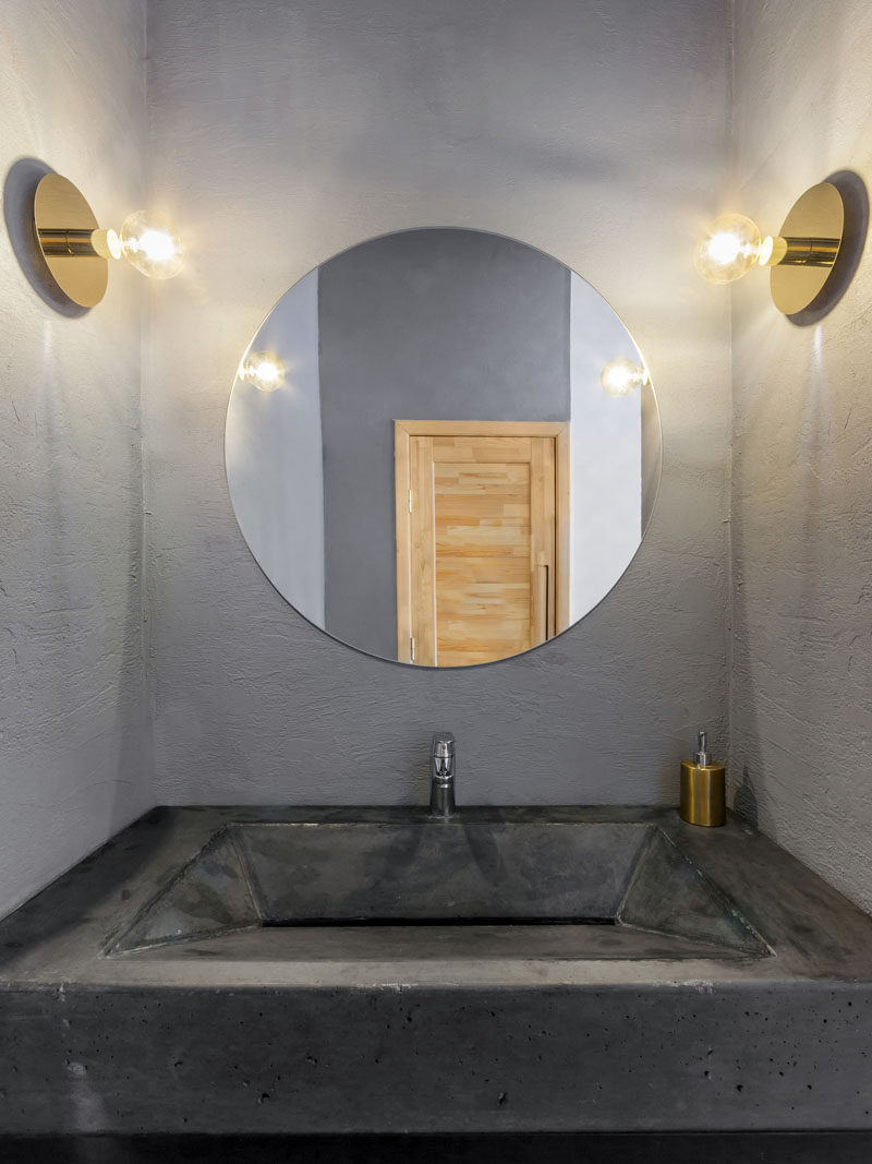 In this modern and simple bathroom, a custom concrete sink fits the space perfectly, gold sconces grace the wall and the round mirror matches the shape of the sconces.