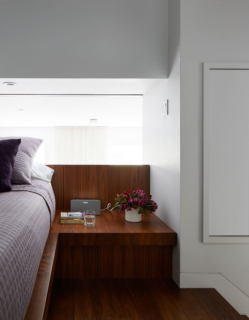 The platform wood bed in this modern loft apartment has built-in side tables and the headboard sits against the guard rail that overlooks the living level below.