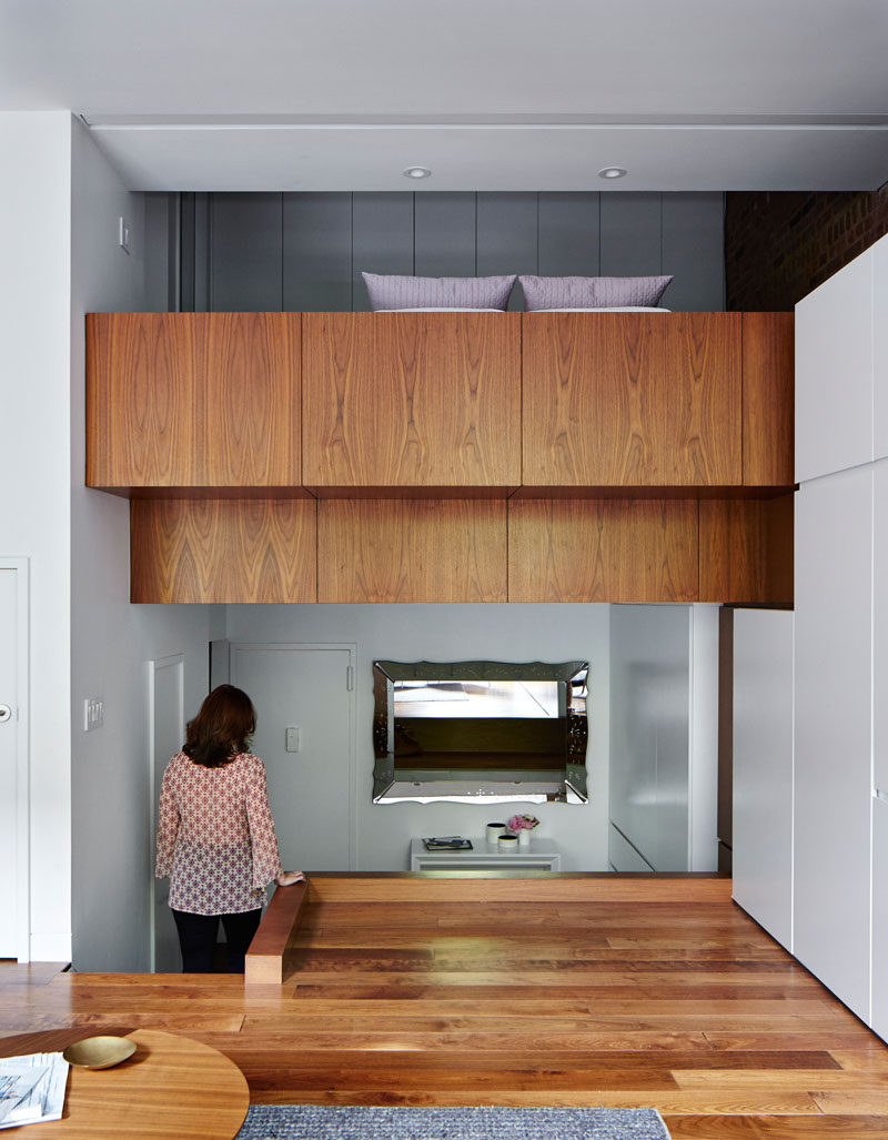 To enlarge the lofted bedroom in this apartment, the sleeping loft was extended out into the living room and covered in walnut paneling, tying in with the flooring.