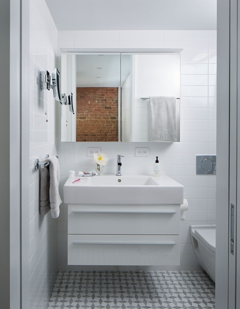 This small bathroom features floor-to-ceiling white tiles, while the mirror reflects the brick on the wall in the bedroom.