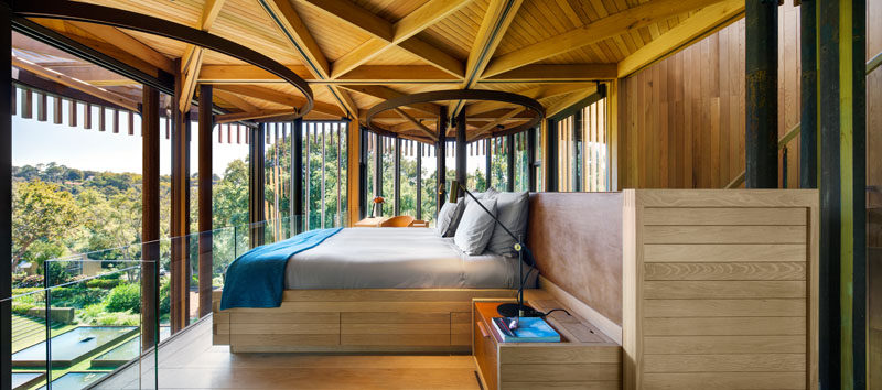 Upstairs in this modern tree house bedroom, a glass safety railing has been added in front of the bed to provide an unobstructed view of the trees.