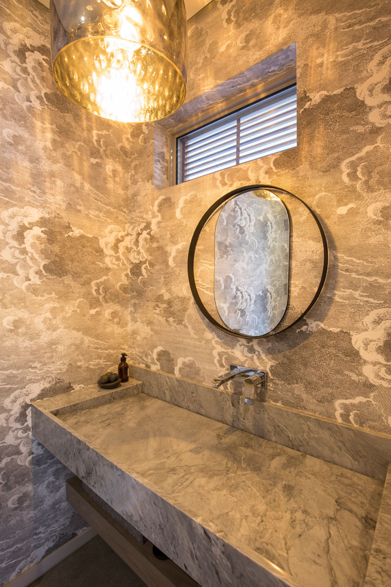 The grey and white cloud wallpaper compliments the large marbled stone inlaid sink, and textured pendant light in this modern bathroom.