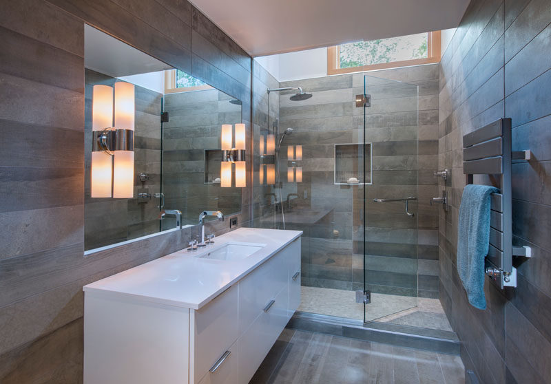 In this modern bathroom, grey tiles adorn the walls, while a glass shower surround allows the light from the window to travel through to the vanity.