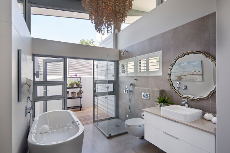 In this modern bathroom, there's a freestanding bathtub, a glass enclosed shower, a large textured chandelier and a private patio that's home to an outdoor shower.