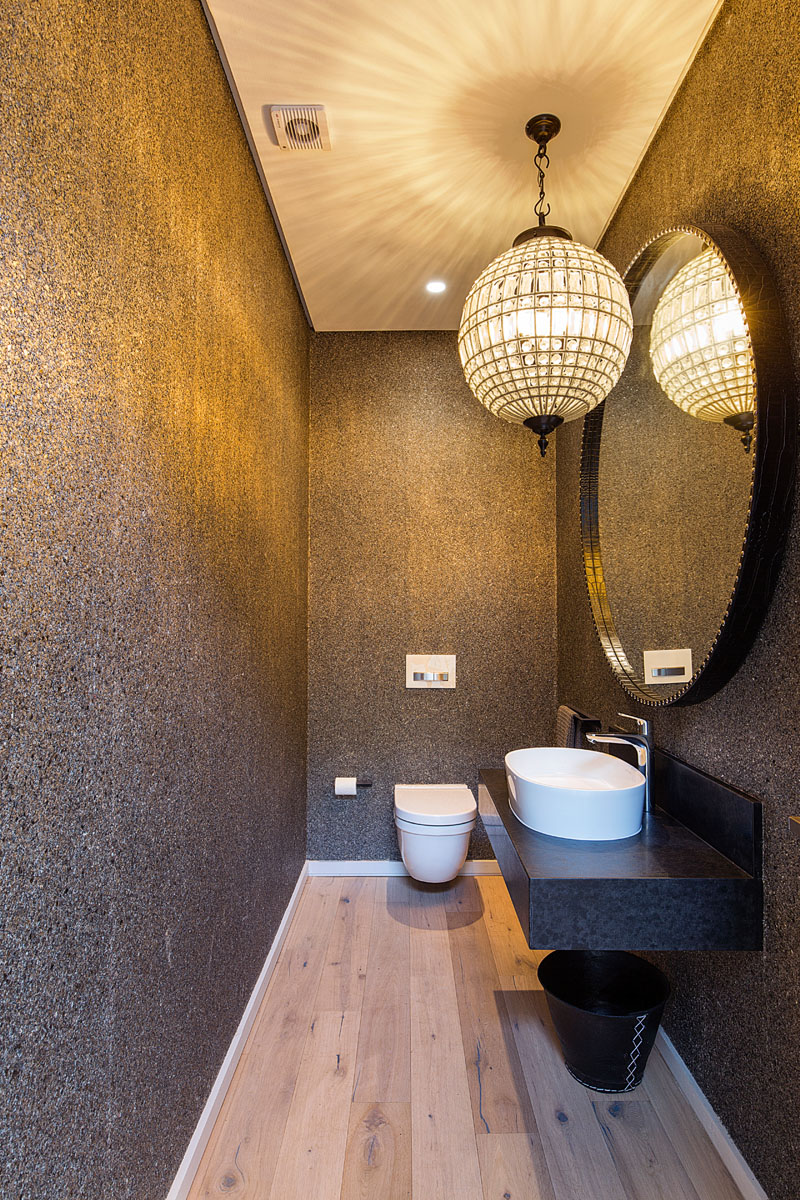 The large glass pendant light in this modern guest bathroom casts shadows onto the ceiling, and gold hues onto the walls.