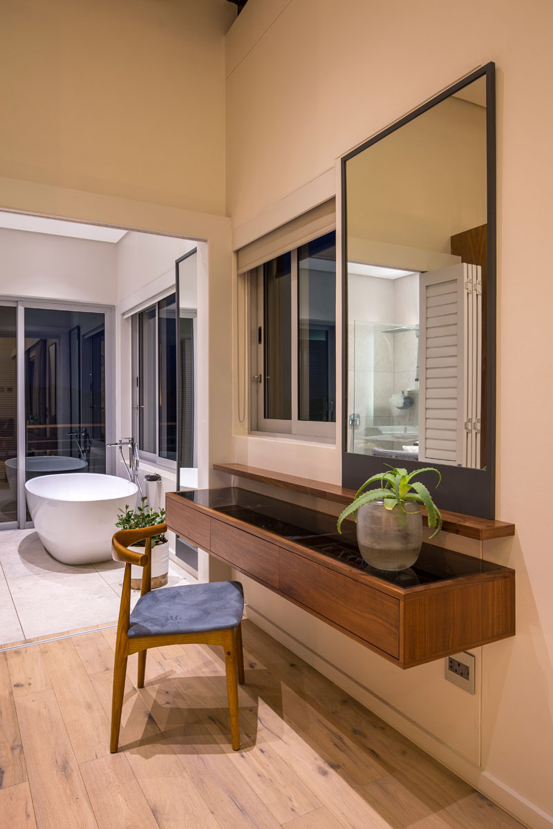 A small space before the walk-in closet and bathroom provides the perfect spot for a modern wood vanity with a large rectangular mirror, and a delicate wood chair.