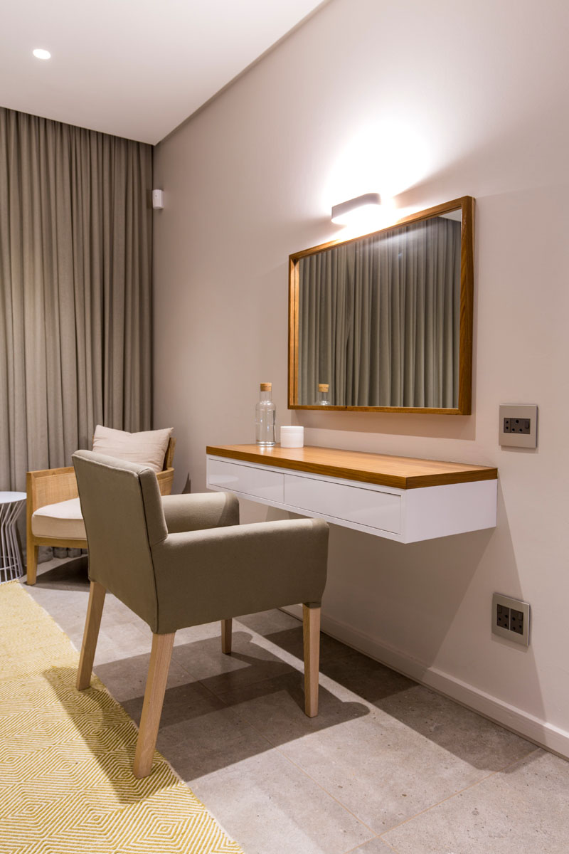 This modern bedroom has a wood framed mirror that hangs above a white vanity/desk that also has a wood top.