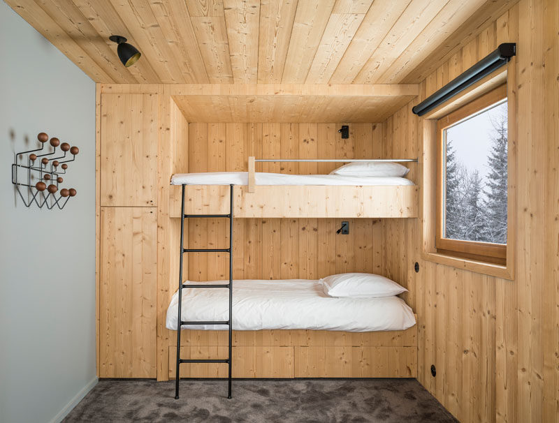 In this rustic modern bedroom, built-in bunk beds with storage cabinets fill one side of the room, while a window adds natural light.