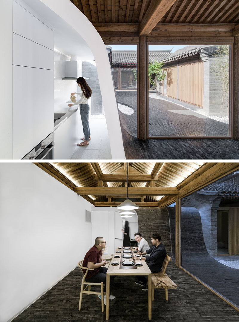 Inside this renovated Chinese building, the small white modern kitchen is tucked behind a curved wall covered in tiles. In the dining area, a long wood table sits below a set of three pendant lights.