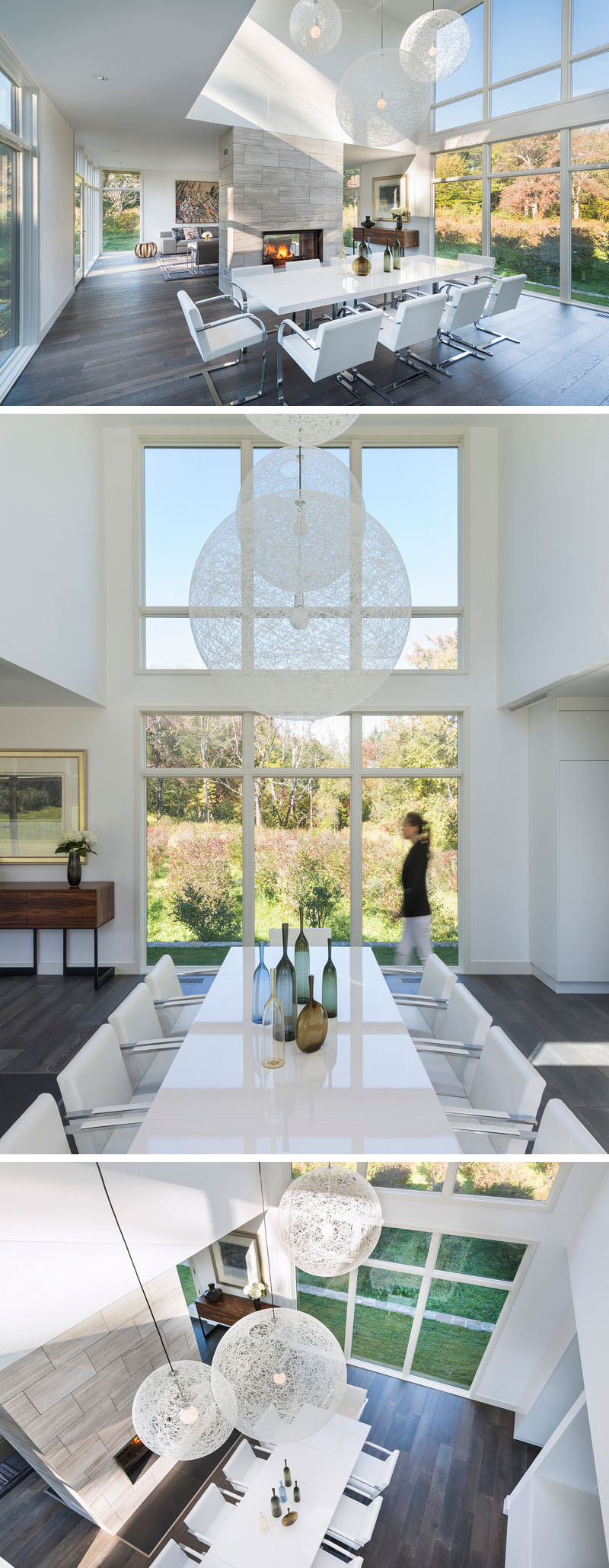 In this modern dining area, three large white pendant lights hang from the double height ceiling in front of floor-to-ceiling windows. A light grey tiled fireplace behind the white dining table separate this space from the living room.