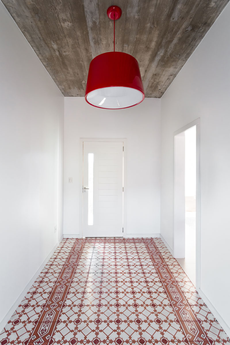 Welcoming you to this modern house is a white entrance hallway, with a bright red pendant lamp and decorative red tiles, and a board-formed concrete ceiling.