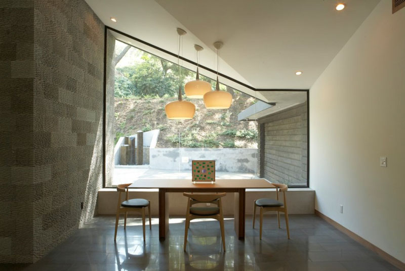 The downward fold in the ceiling of this modern home gives the black framed window a unique shape. 