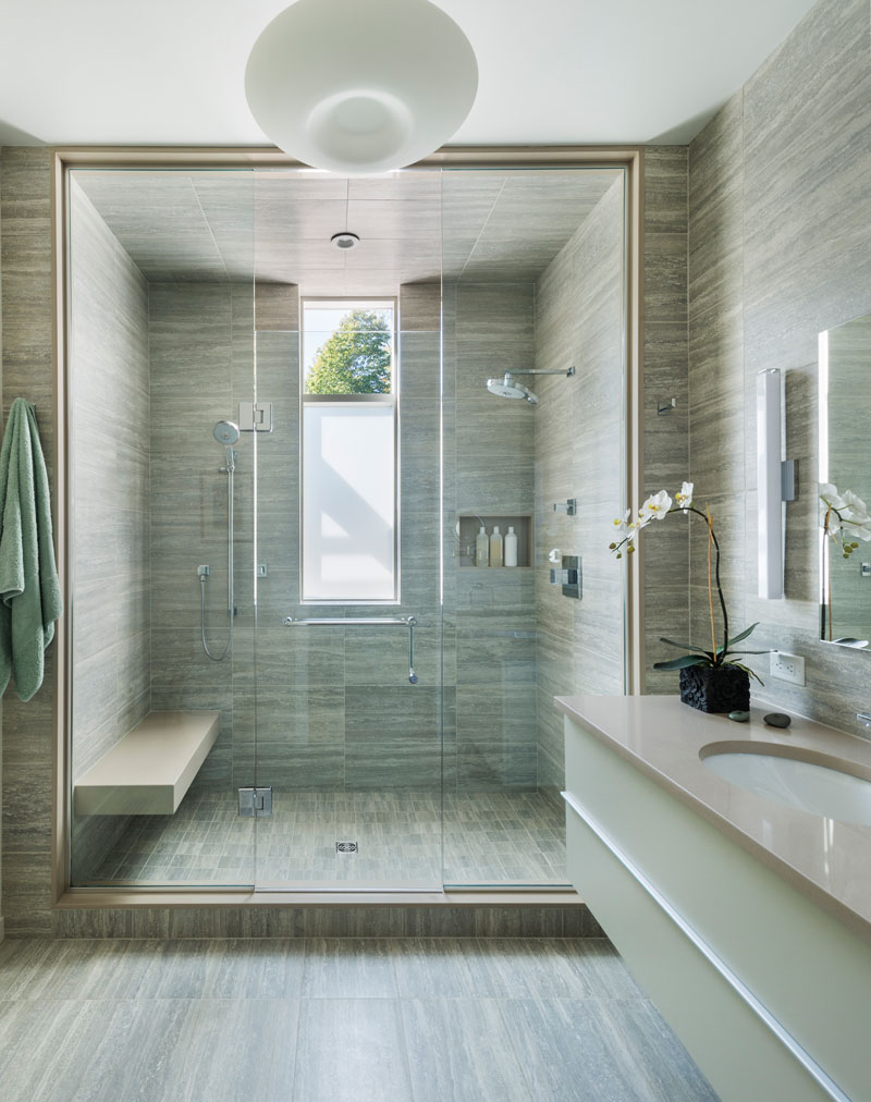  In this modern bathroom, a large walk-in shower has double shower heads and a built-in bench, while the same tile used in the shower has also been used for the walls and floor.