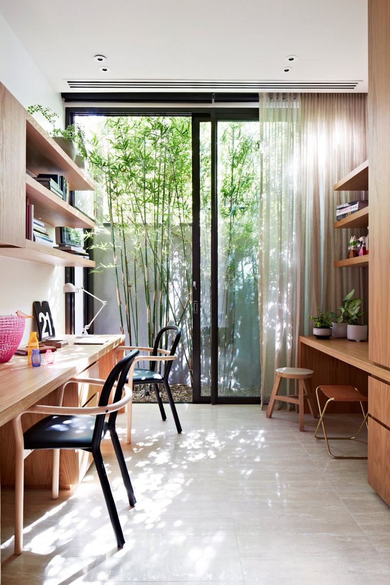 Light and airy, this home office has easy access to outside via the patio door and ample room for multiple people work. Light wood is used on either side of the room for open shelving, storage and functional work space.