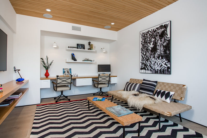 Tucked in at the back of this living room, is a shared home office or homework station. For extra lighting, the built-in wood desk has white lights that hang above each work area.