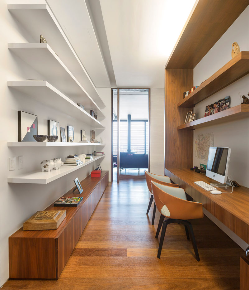 In this home office built for two, wood shelving and long desk are on one side, while floating white shelves for books and decorative displays sit on the opposite wall.